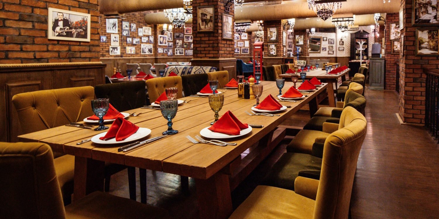 a restaurant hall with red brick walls wooden tables and pipes in the ceiling